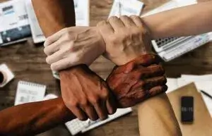 Arms and hands of different races joined together across a desk, symbolizing diversity in the workplace and DEI metrics.